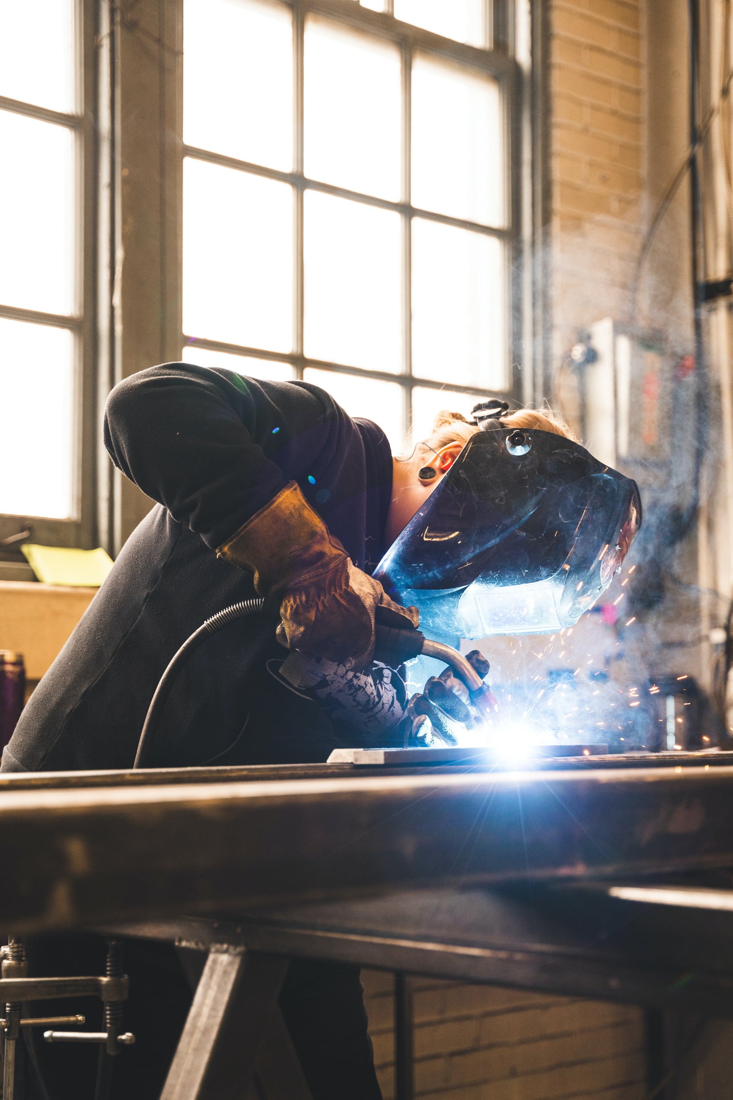 Professional welder using a MIG torch on a steel workpiece in a workshop